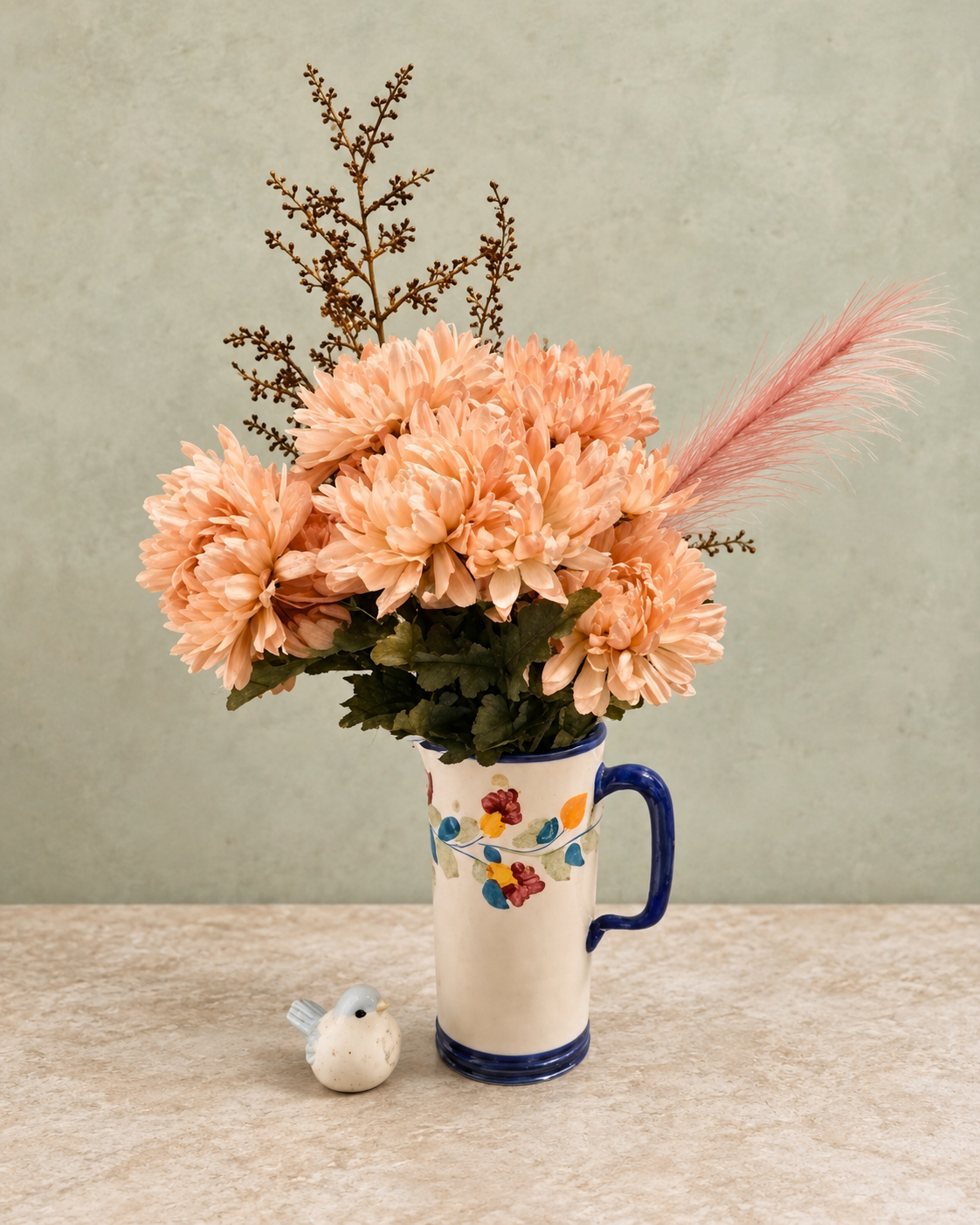 Peach flowers in a blue-handled floral pitcher, shown complete with top branches and a small bird