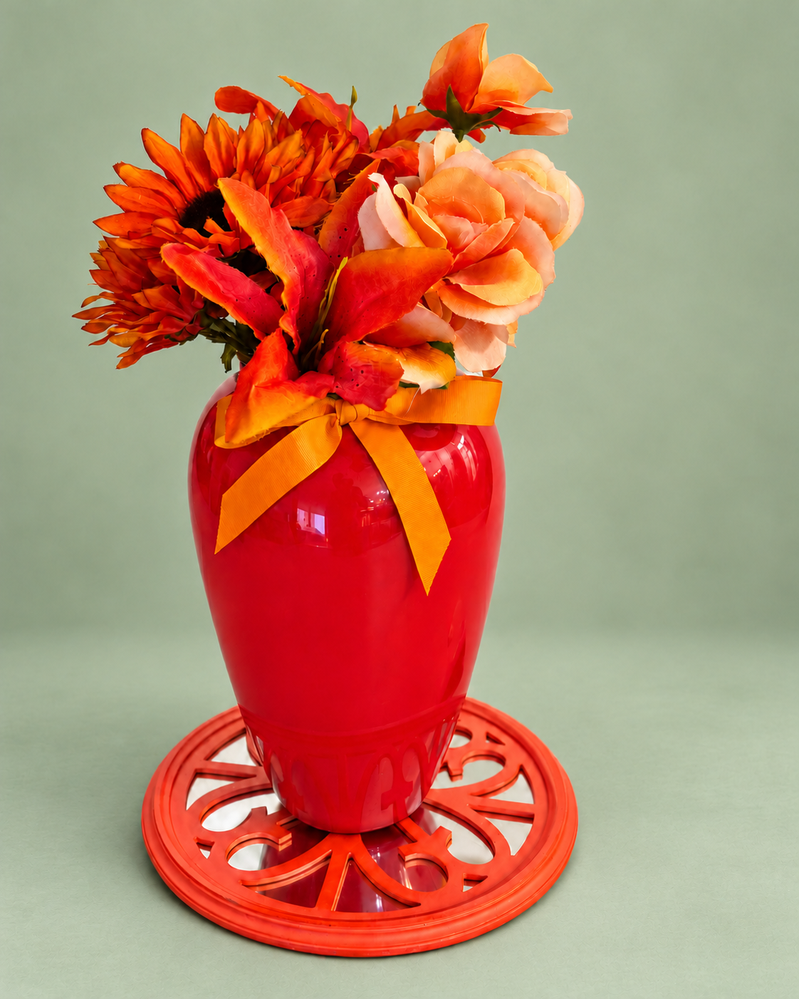 Autumn flowers in a tall glossy red vase with orange ribbon on a soft sage green background